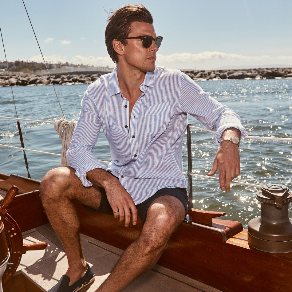 EDITORIAL IMAGE OF MODEL SITTING ON A SAIL BOAT WEARING CONNOR SHIRT IN DENIM WHITE RAILROAD. 